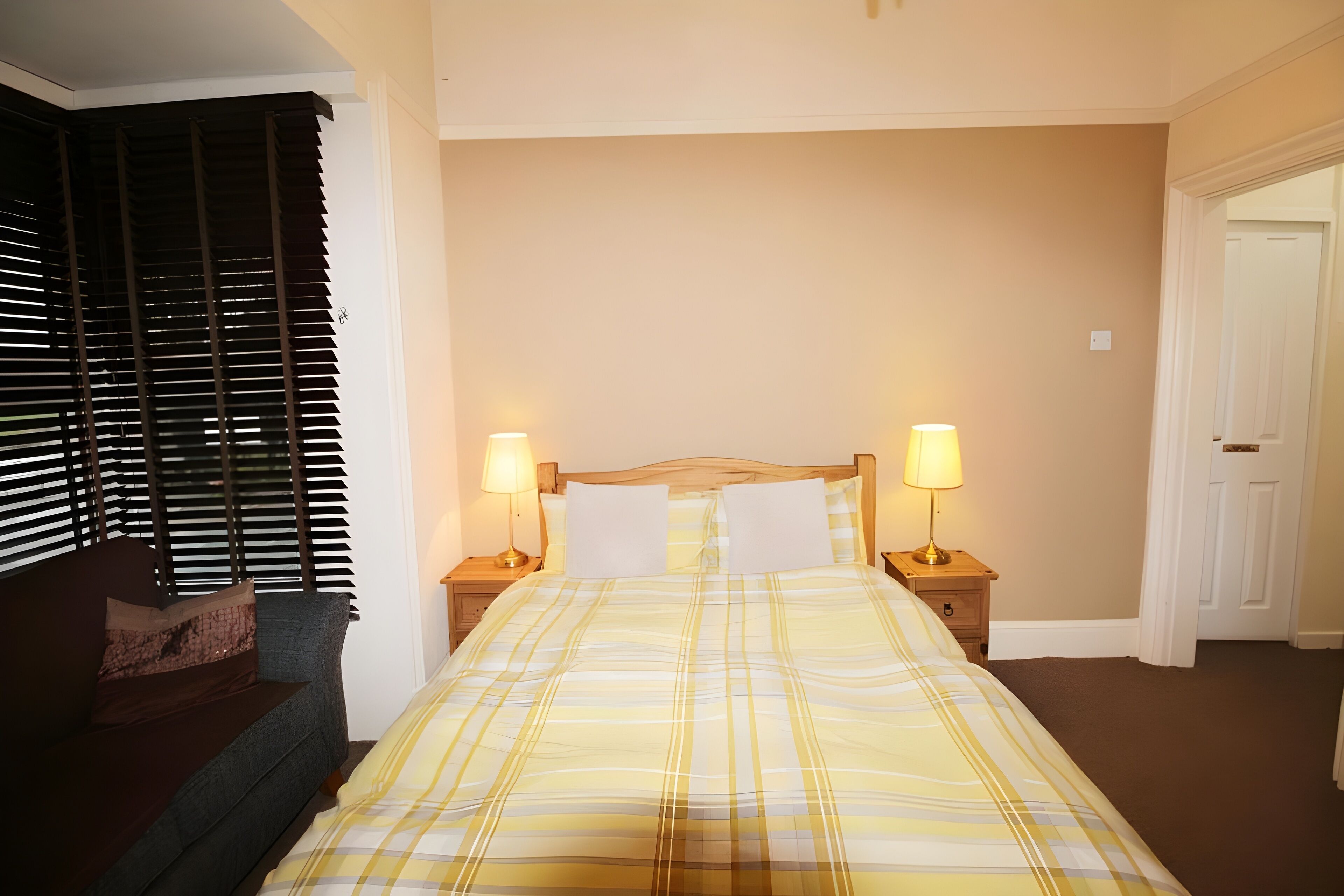 A bedroom with a bed, two bedside lamps, a nightstand, a sofa, and a window with blinds.