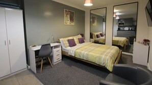 Un dormitorio con cama, escritorio, silla, armario y espejo.