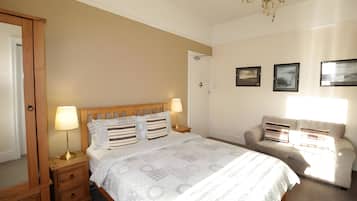 A bedroom with a bed, bedside tables, a dresser, a sofa, and a chandelier.