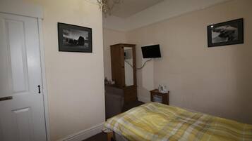 Een slaapkamer met een bed, een dressoir, een spiegel en twee televisies aan de muur.