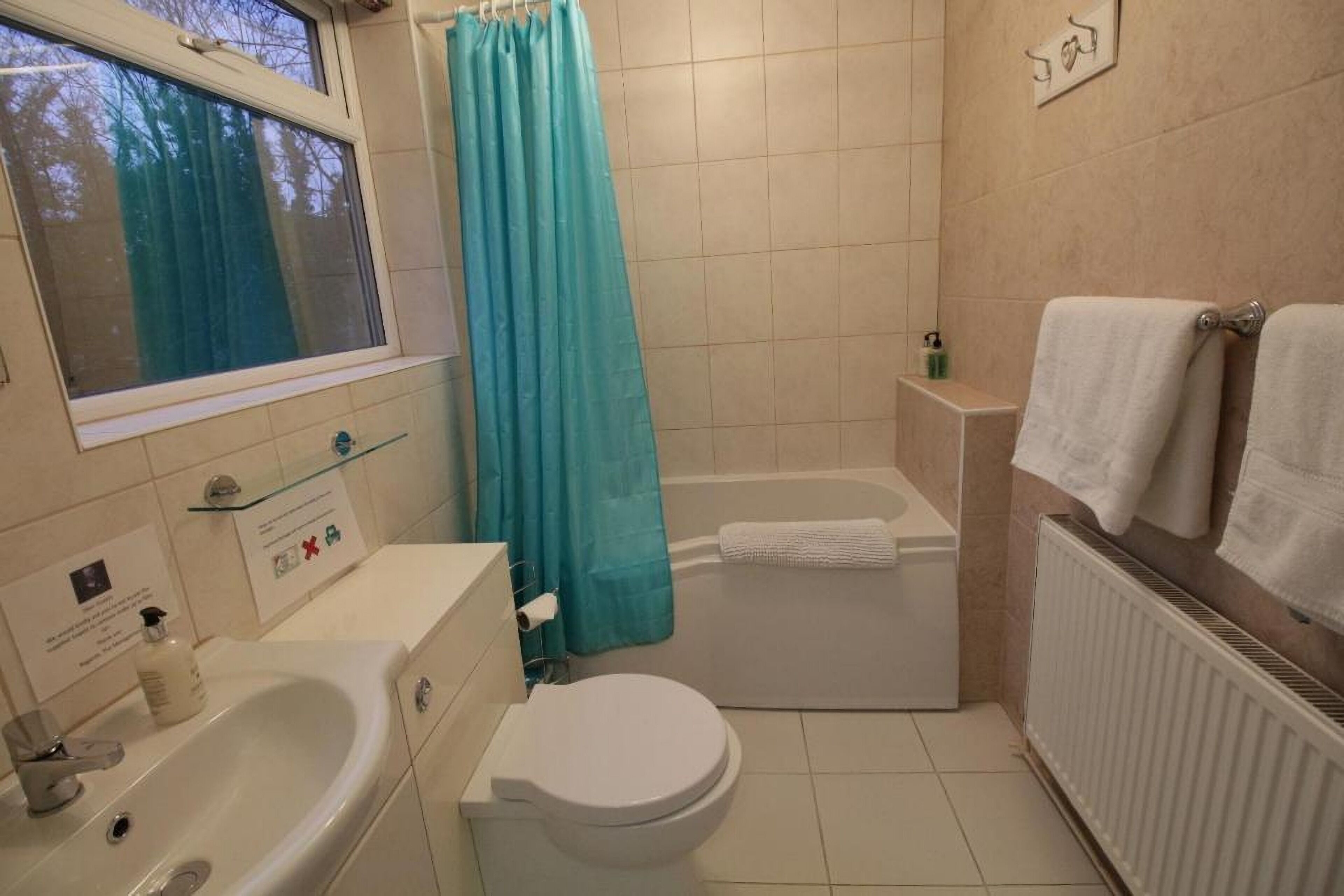 Ein Badezimmer mit Badewanne, Toilette, Waschbecken und einem Fenster mit Blick auf Bäume.