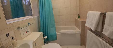 Ein Badezimmer mit Badewanne, Toilette, Waschbecken und einem Fenster mit Blick auf Bäume.
