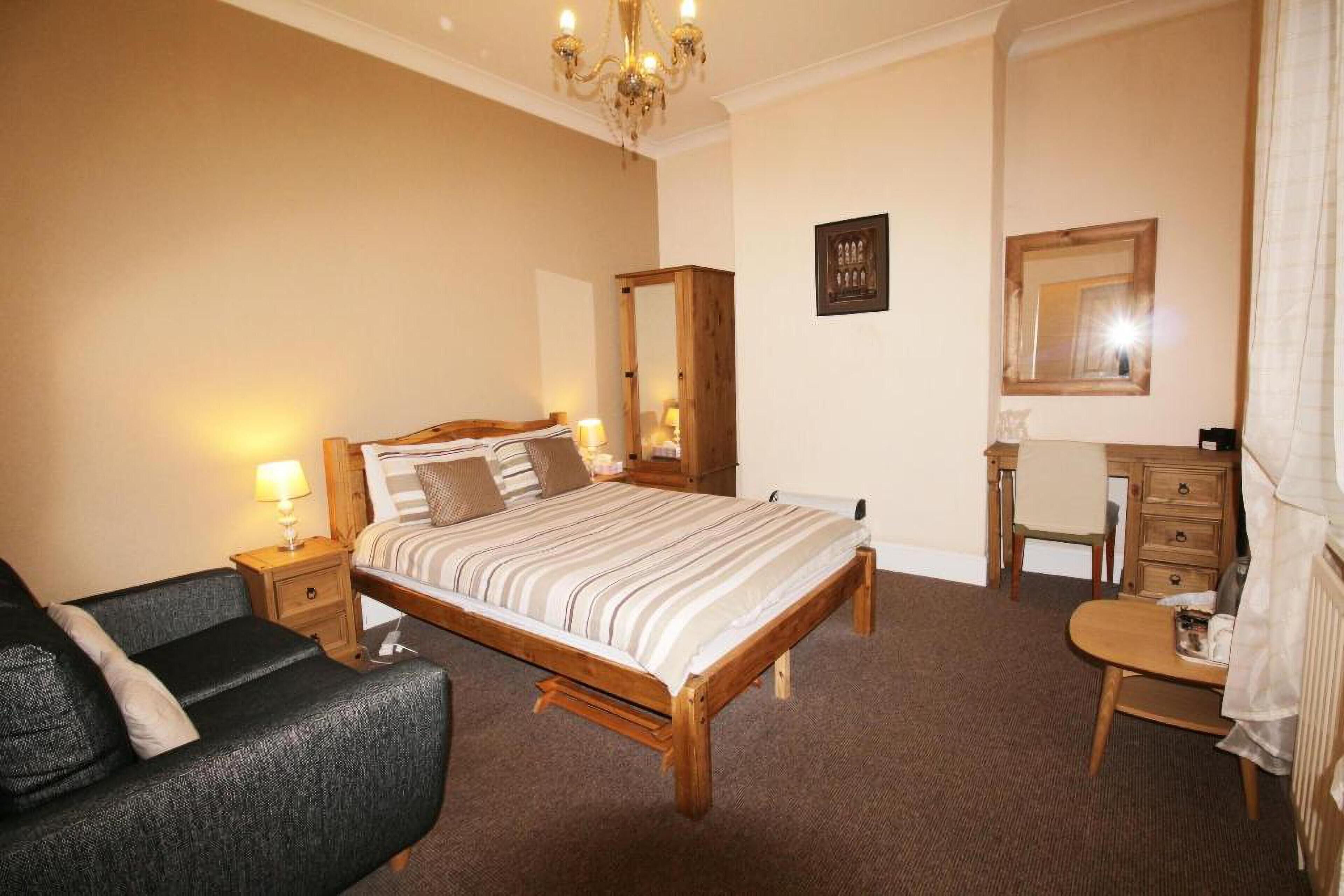 A bedroom with a wooden bed, a small desk, a chair, a dresser, a mirror, and a chandelier.
