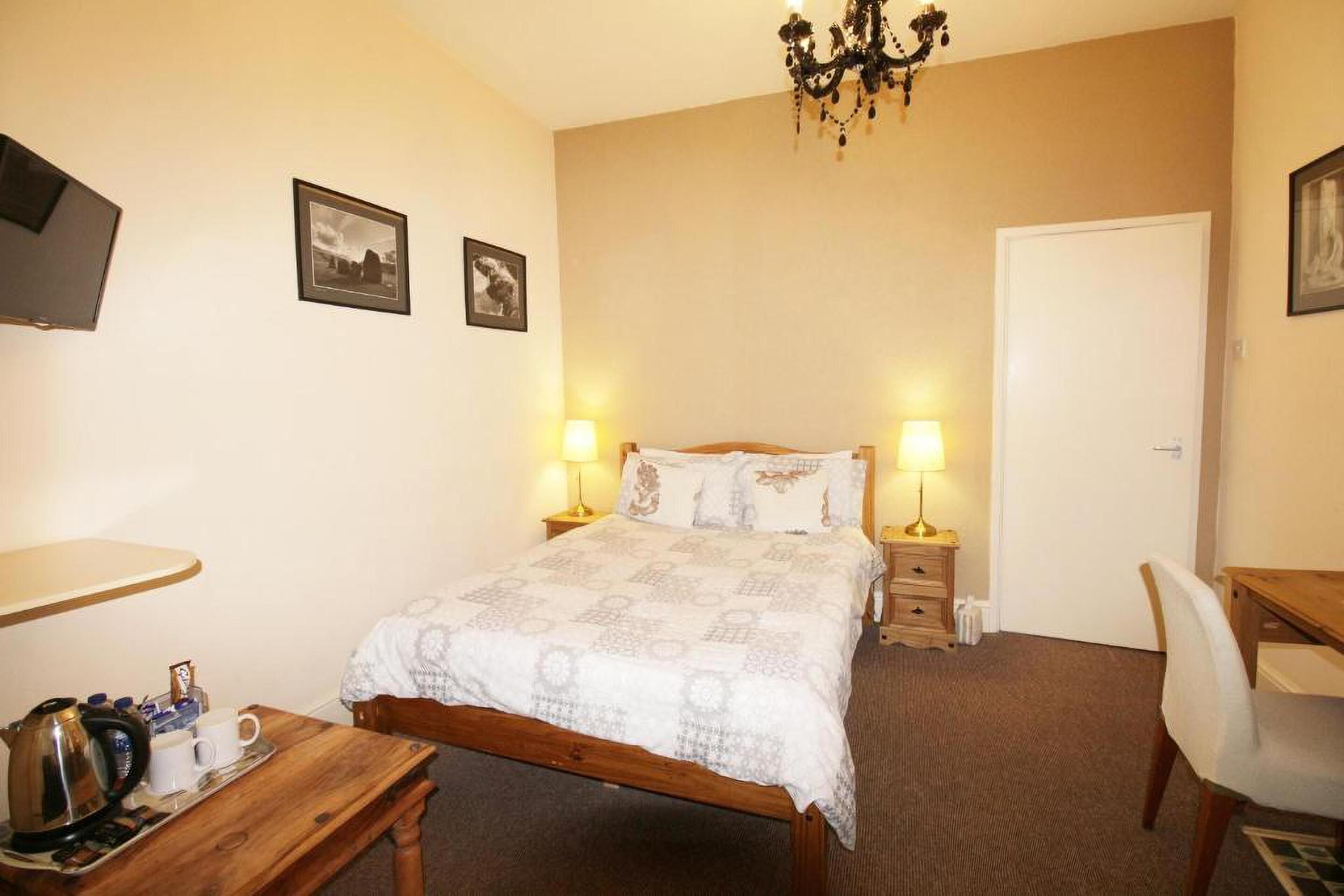A bedroom with a bed, bedside lamps, a desk, and a chair.