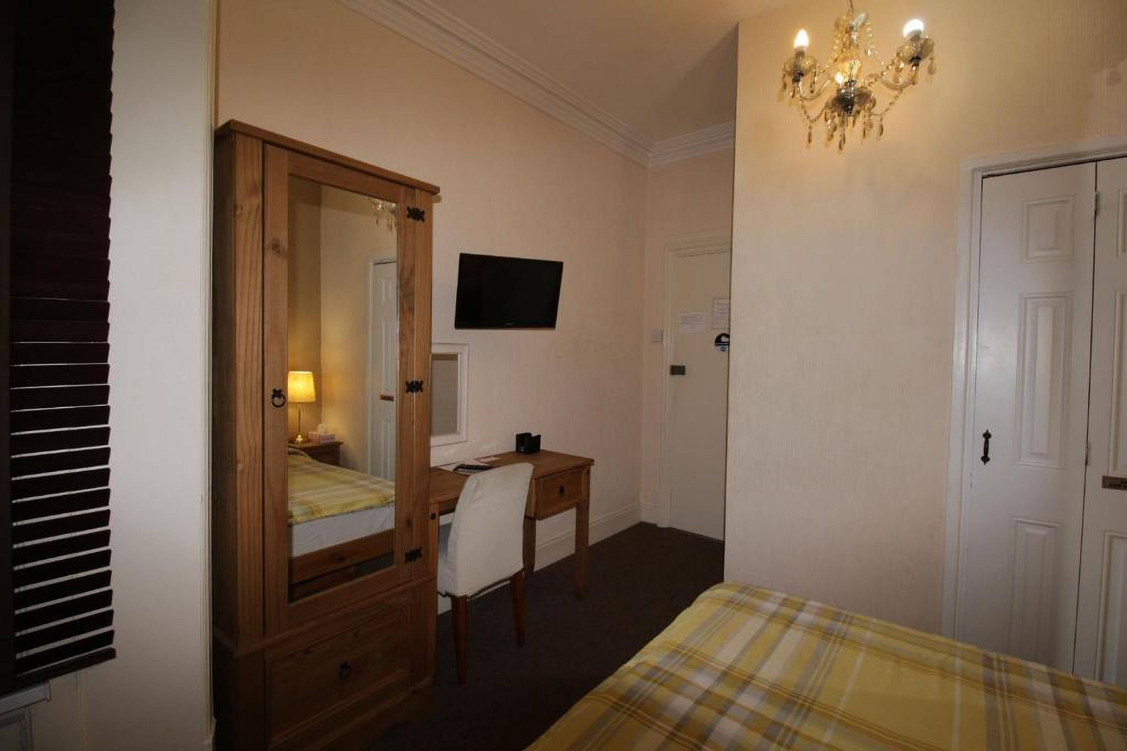 Ein Schlafzimmer mit einem Bett, einer Holzkommode, einem Schreibtisch, einem Sessel, einem Fernseher und einer Kristallleuchtre.