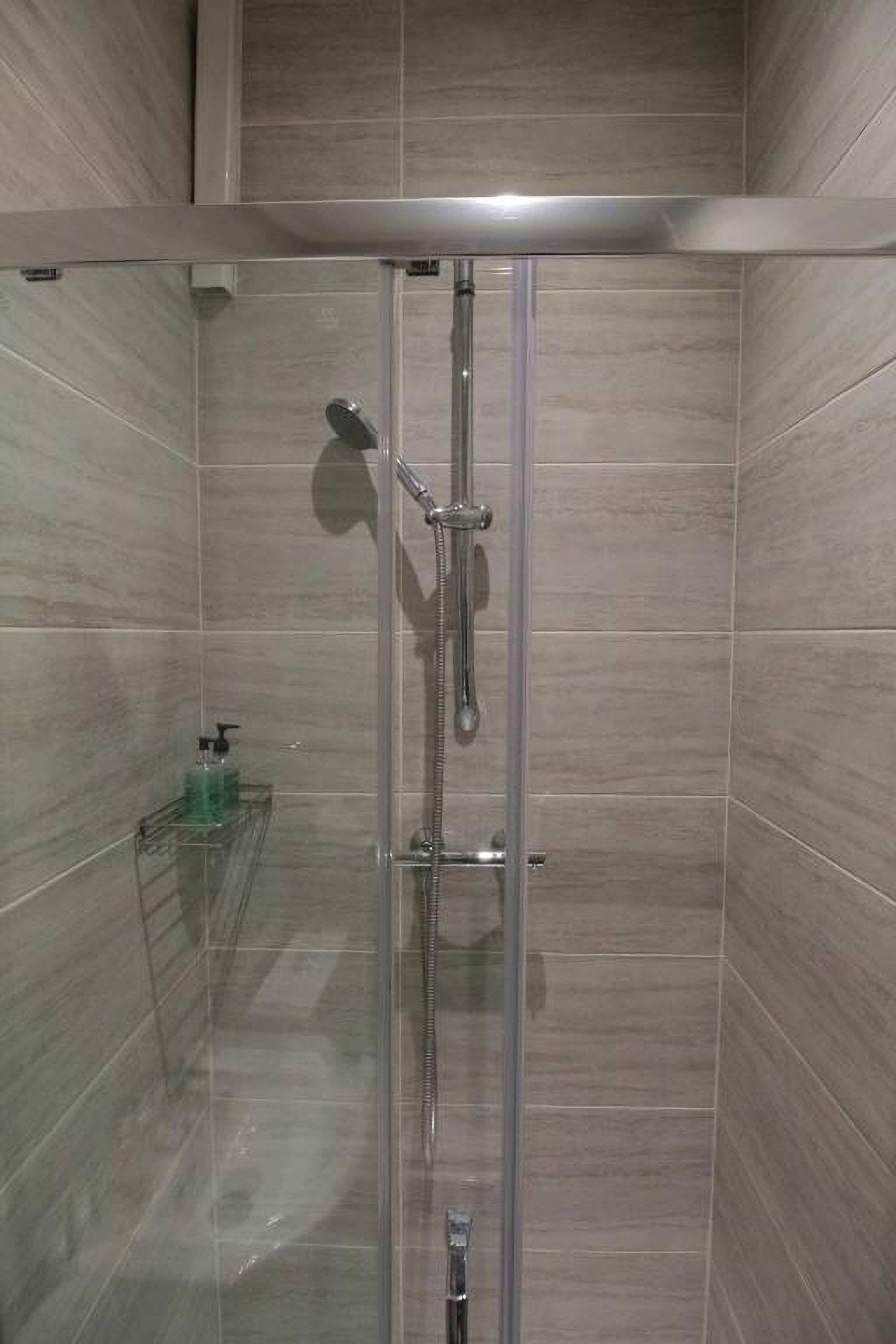 A glass-enclosed shower stall with a handheld showerhead and a wall-mounted faucet.