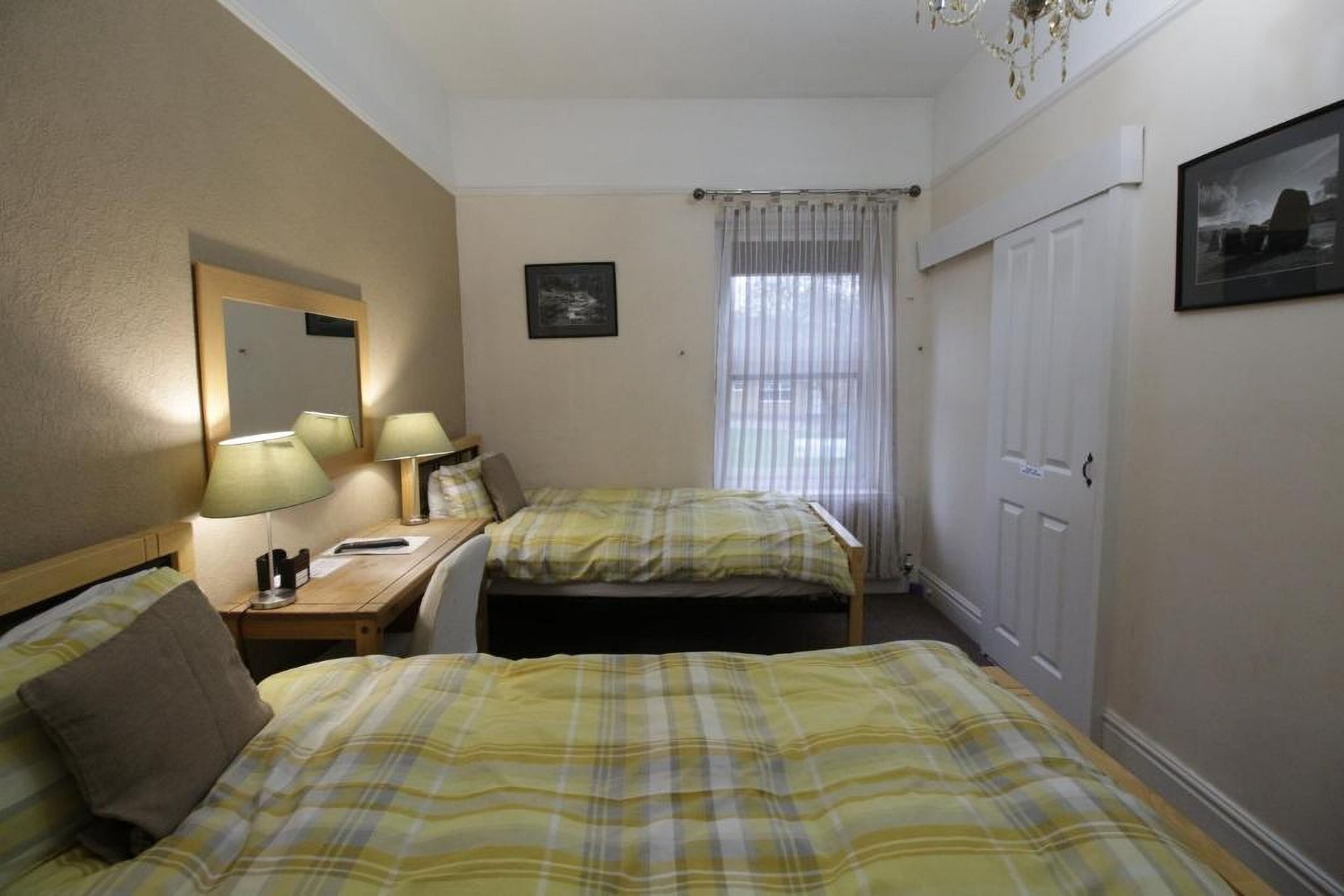 Une chambre d’hôtel avec deux lits, un bureau avec une lampe, un miroir, une fenêtre avec des rideaux et une porte.