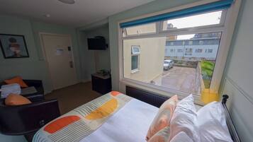 A hotel room with a bed, a desk, a chair, a television, and a window with a view of the outside.