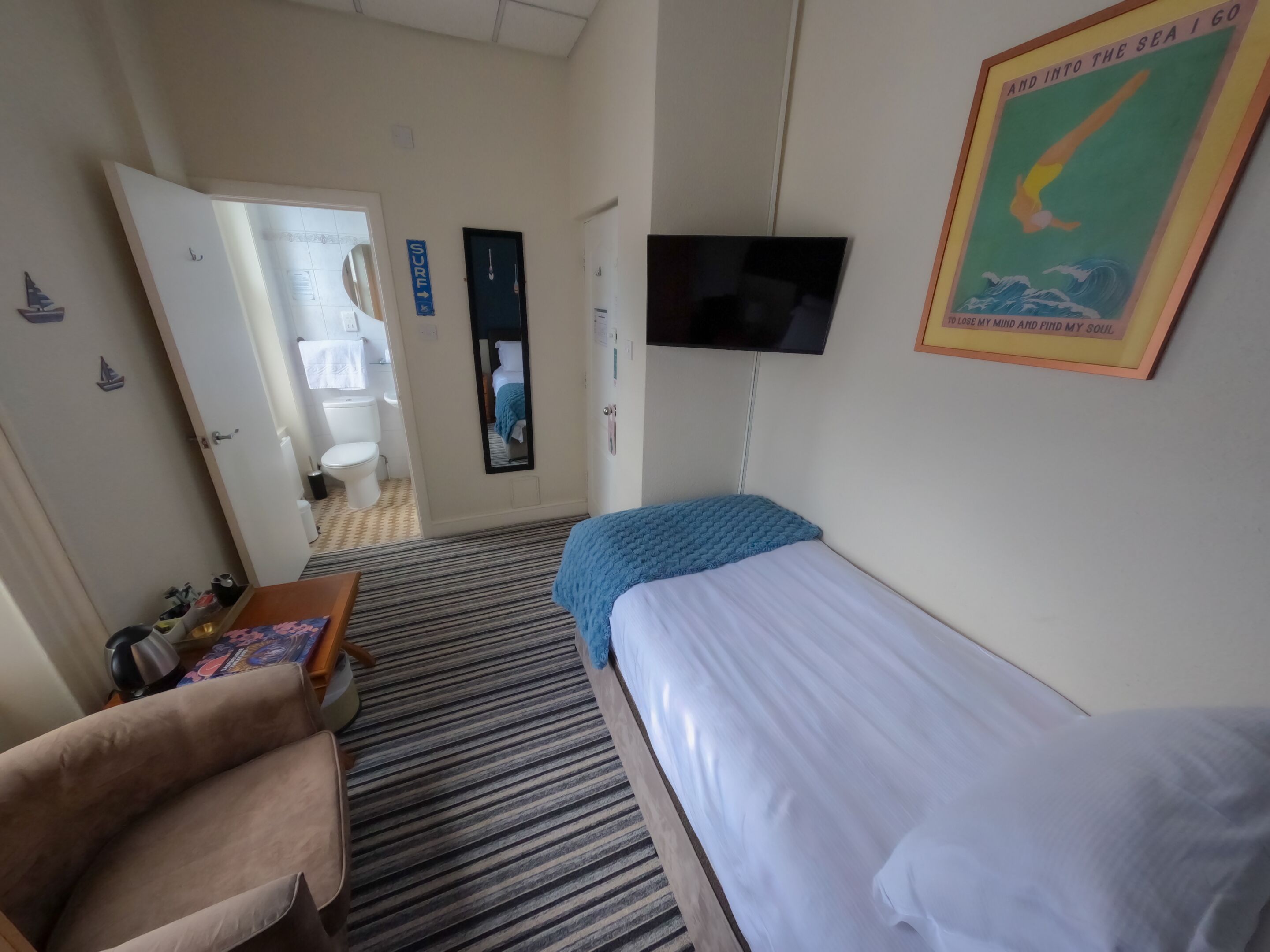 A hotel room with a bed, a TV, a chair, and a small table.