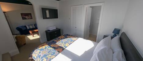 A bedroom with a bed, a dresser, a nightstand, a lamp, and a door leading to a bathroom.