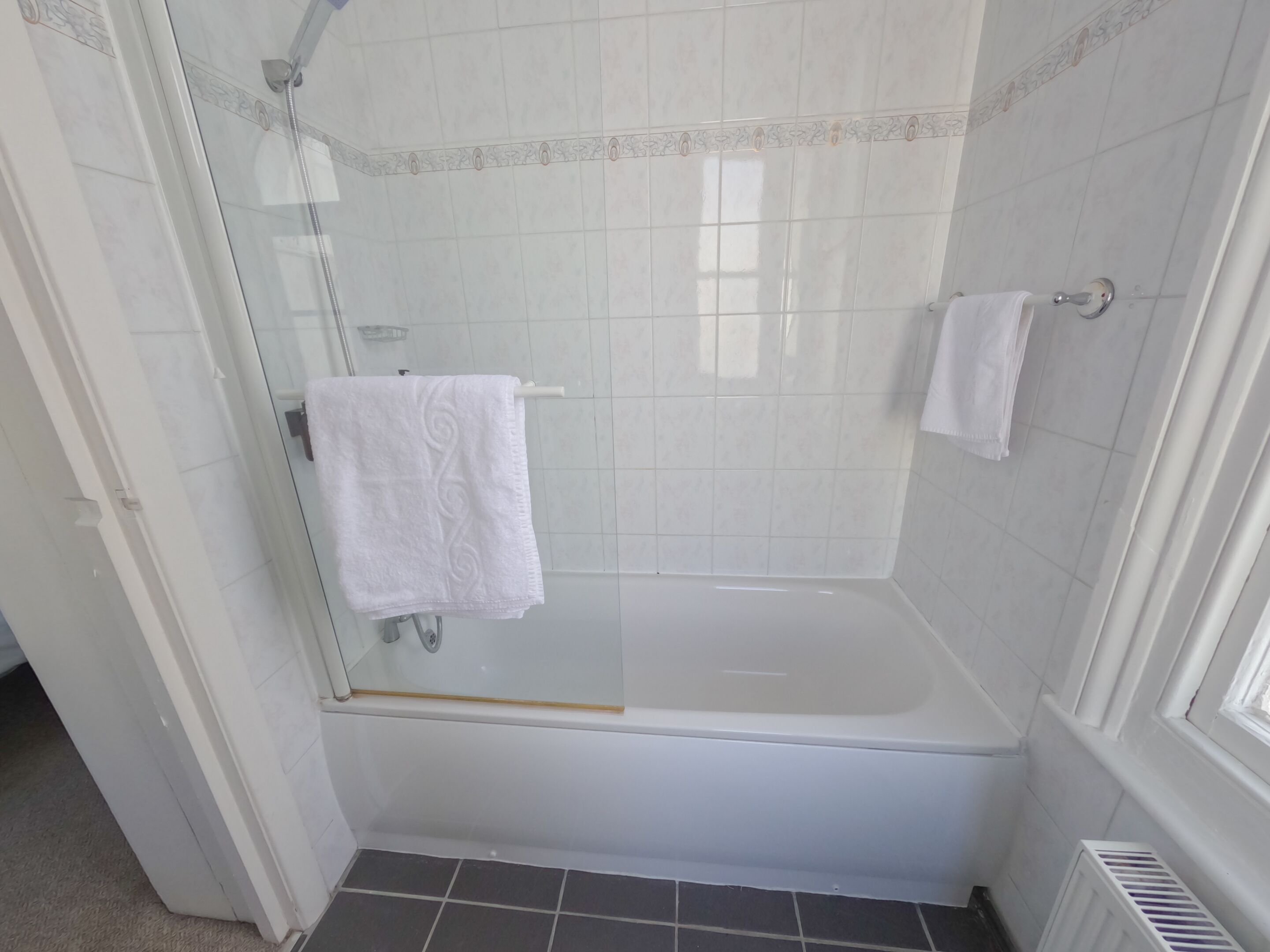 Ein Badezimmer mit einer Duschkabine, einer weißen Badewanne und einem weißen Handtuch an einem Haken.