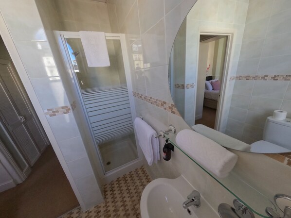 Casa de banho com chuveiro em cabine de vidro, lavatório de vidro e sanita.