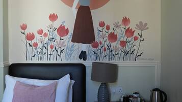 A bedroom with a bed, a dresser, a lamp, and a wall mural.