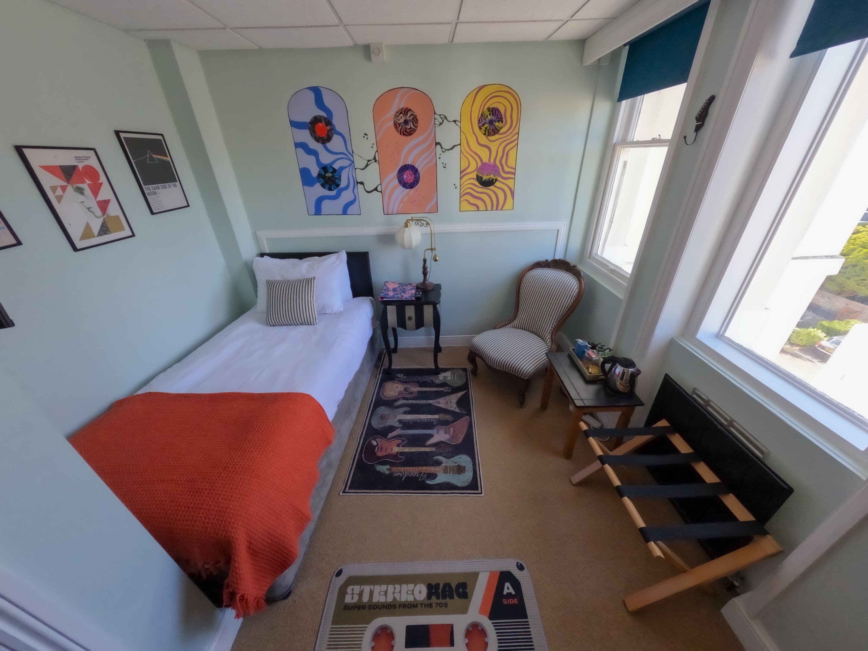 Een slaapkamer met een bed, een stoel, een klein tafeltje, een raam en wanddecoratie.