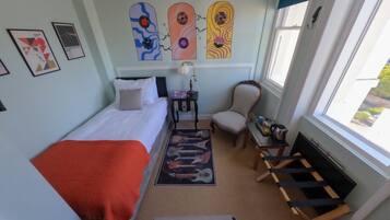 Een slaapkamer met een bed, een stoel, een klein tafeltje, een raam en wanddecoratie.