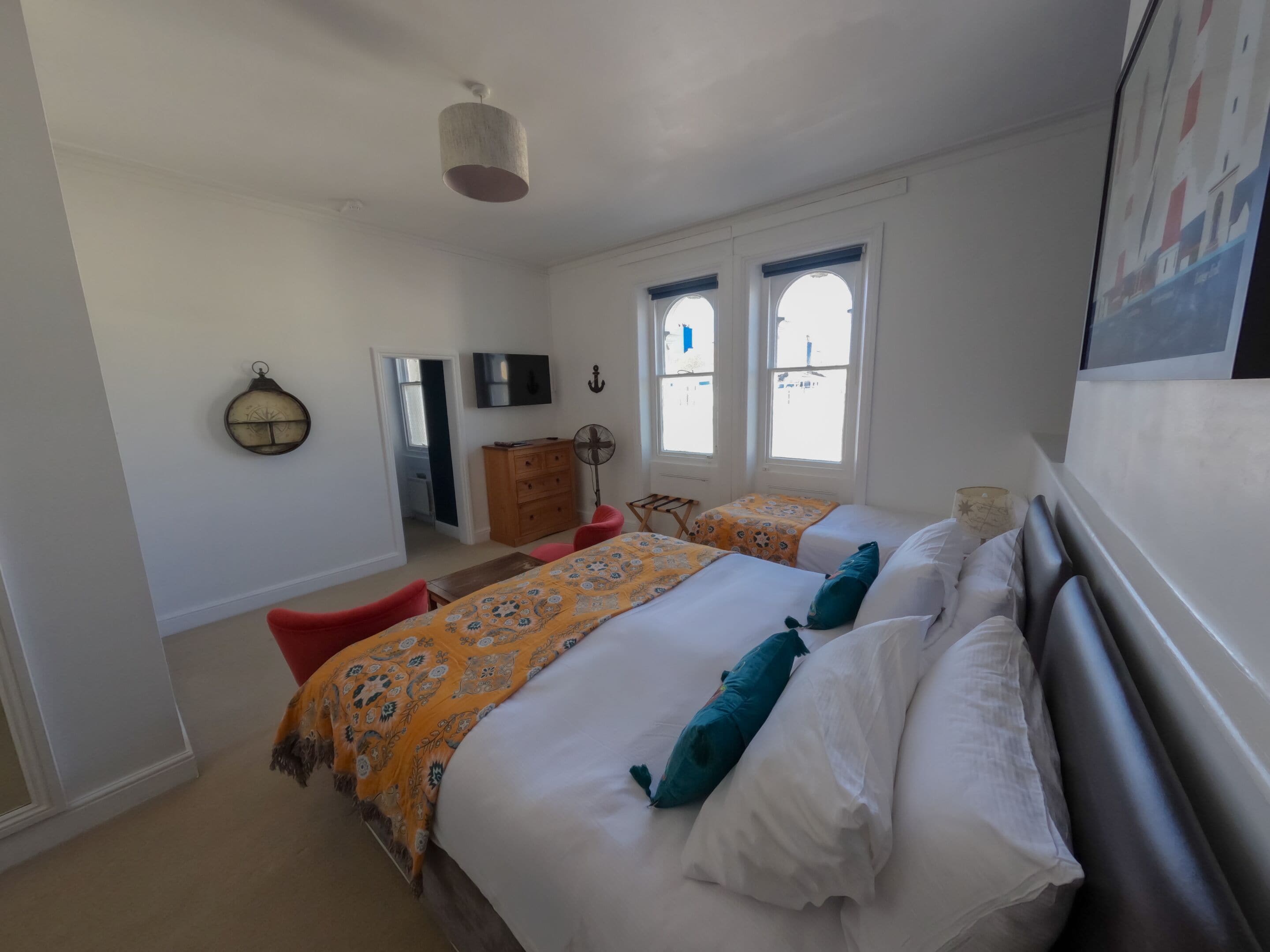 Une chambre avec deux lits, une télévision, une commode en bois et un ventilateur.