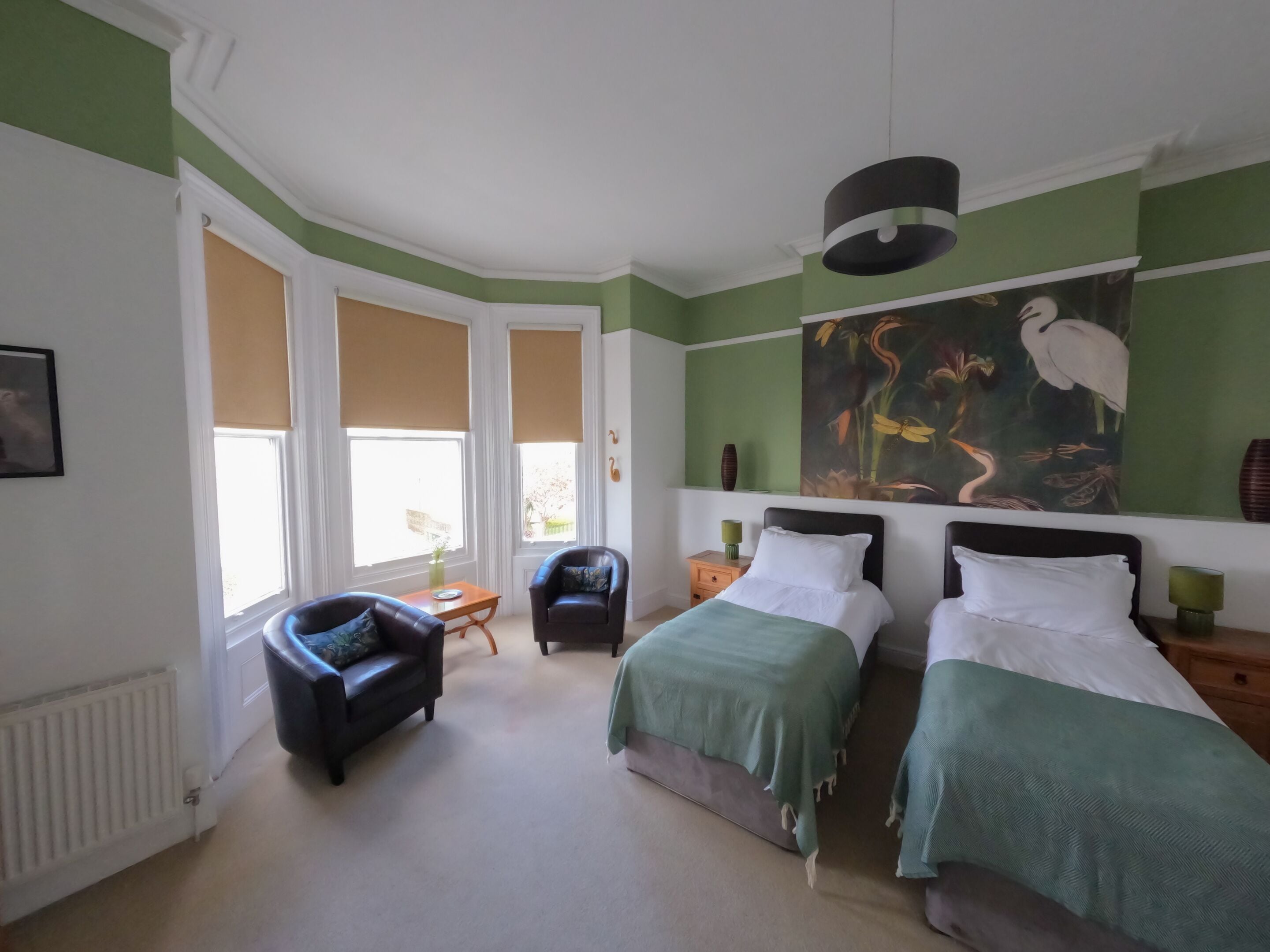 A bedroom with two beds, a chair, a table, and a large painting on the wall.