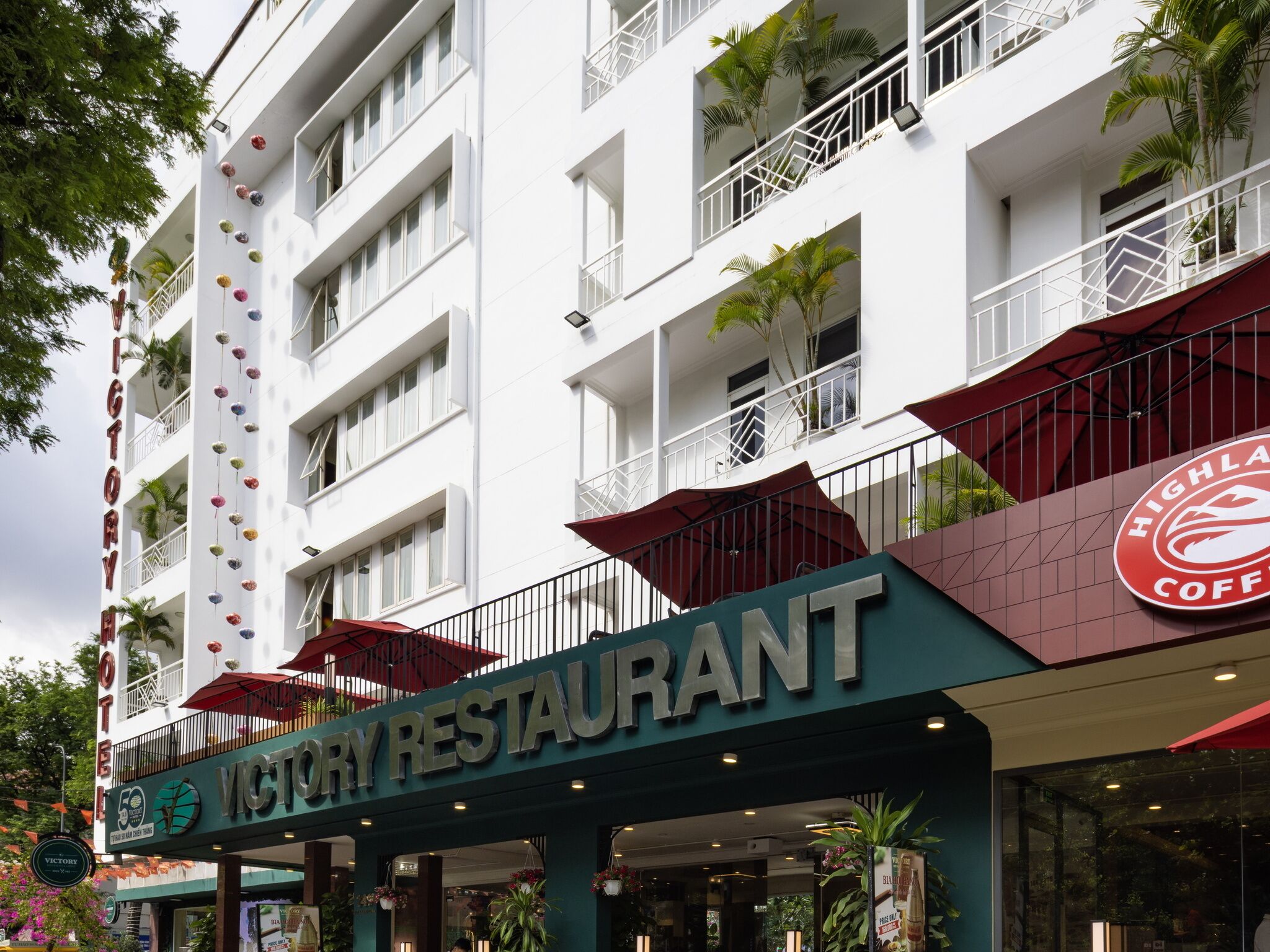 A hotel with a restaurant on the ground floor, balconies with umbrellas, and a sign for Highland Coffee.