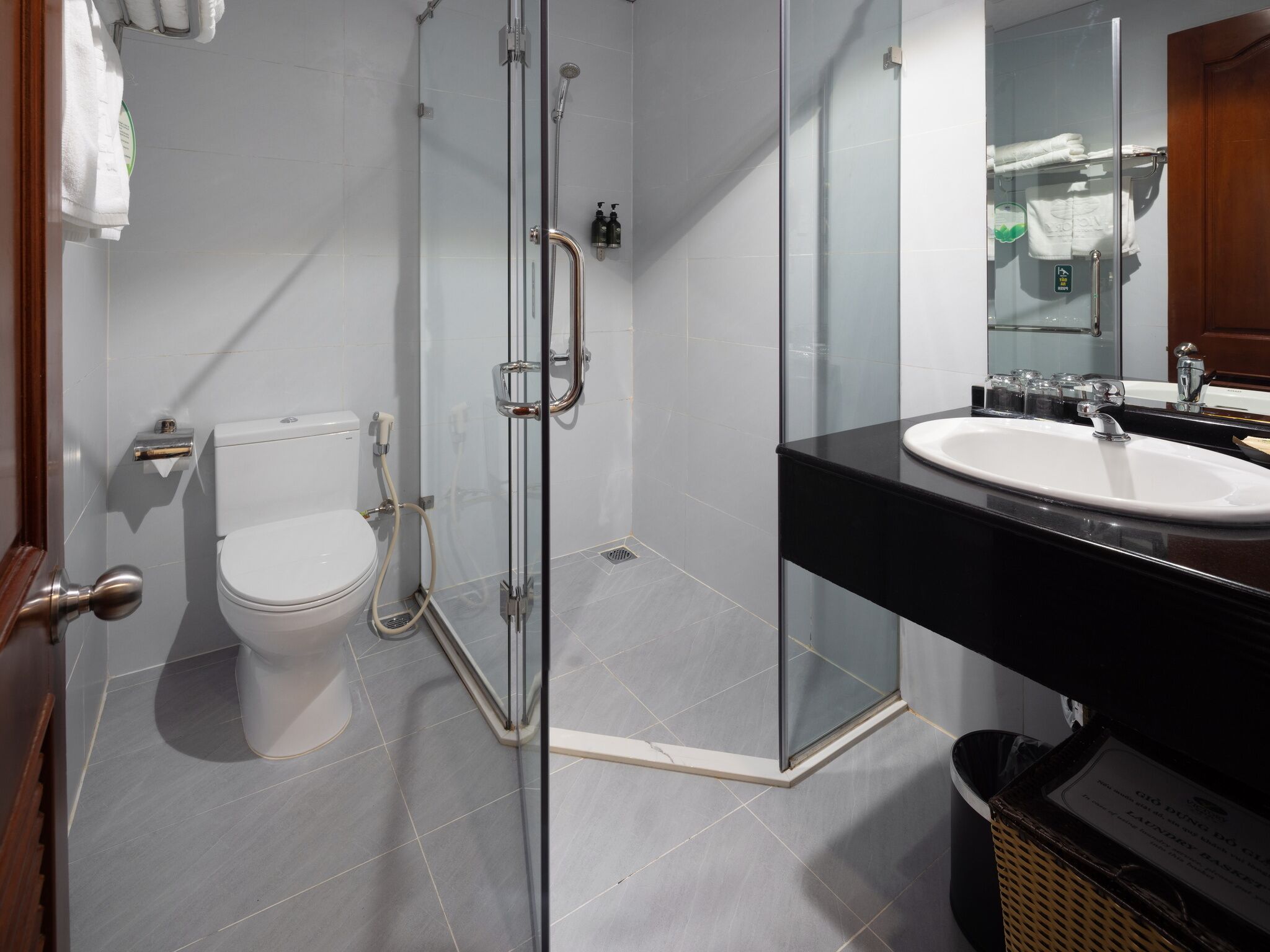 Un baño moderno con cabina de ducha de vidrio, inodoro blanco y lavamanos negro con espejo superior.
