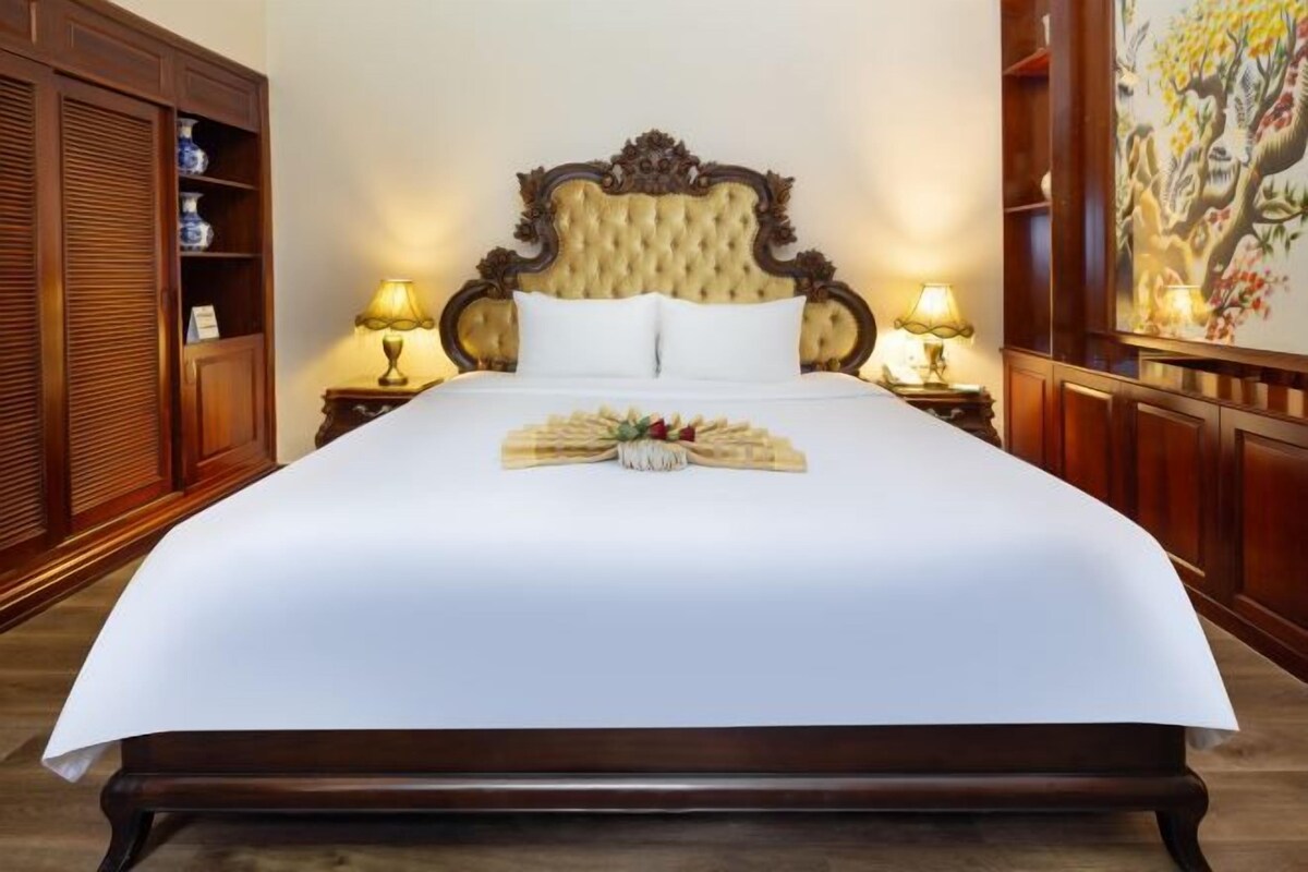 Uma cama grande com cabeceira estofada, duas luminárias de apoio e um tabuleiro decorativo sobre a cama.