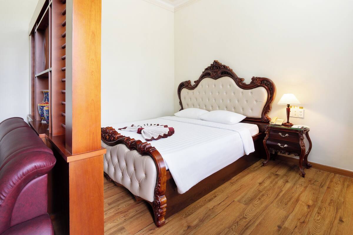 A neatly made bed with a wooden headboard, a bedside table with a lamp, and a red leather chair.