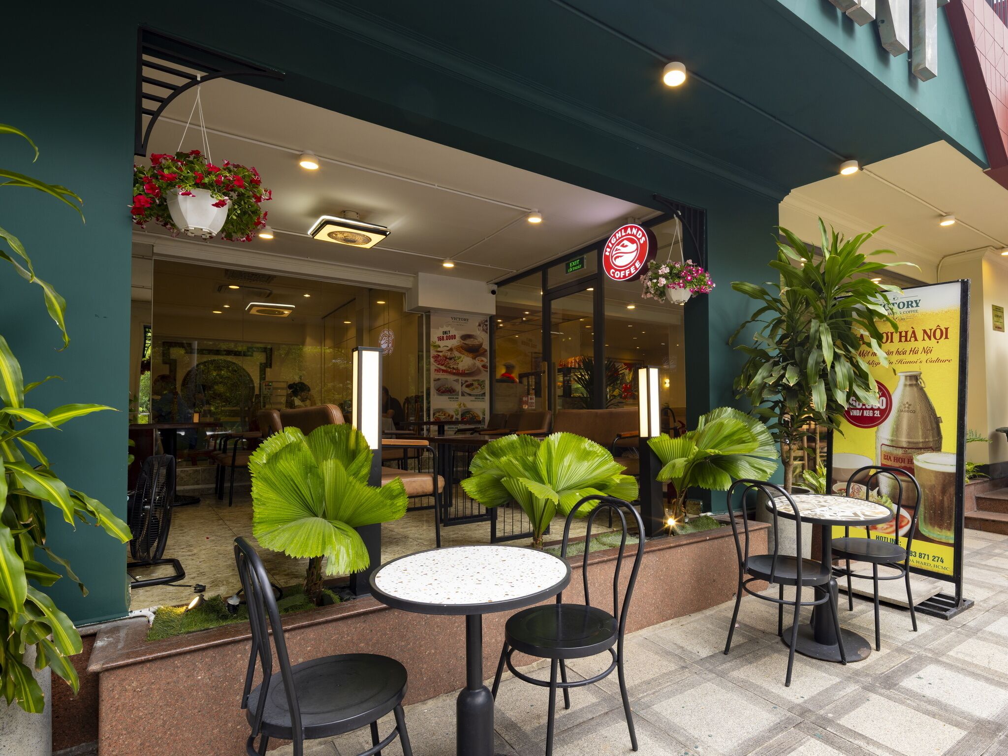 An outdoor cafe area with tables and chairs, a hanging flower basket, and a sign for Highland Coffee.