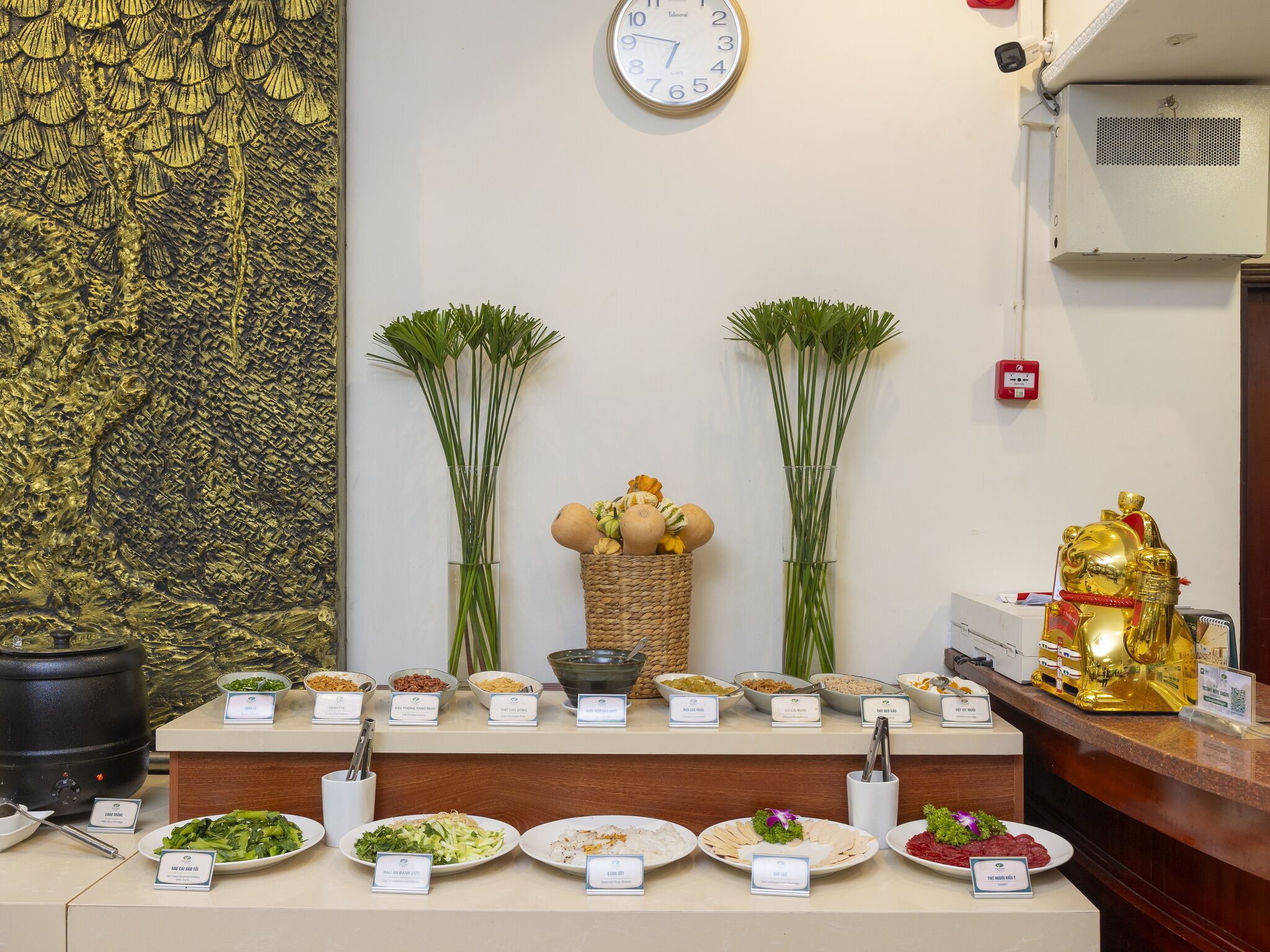 A buffet area with various dishes labeled, a clock on the wall, and a decorative golden statue.
