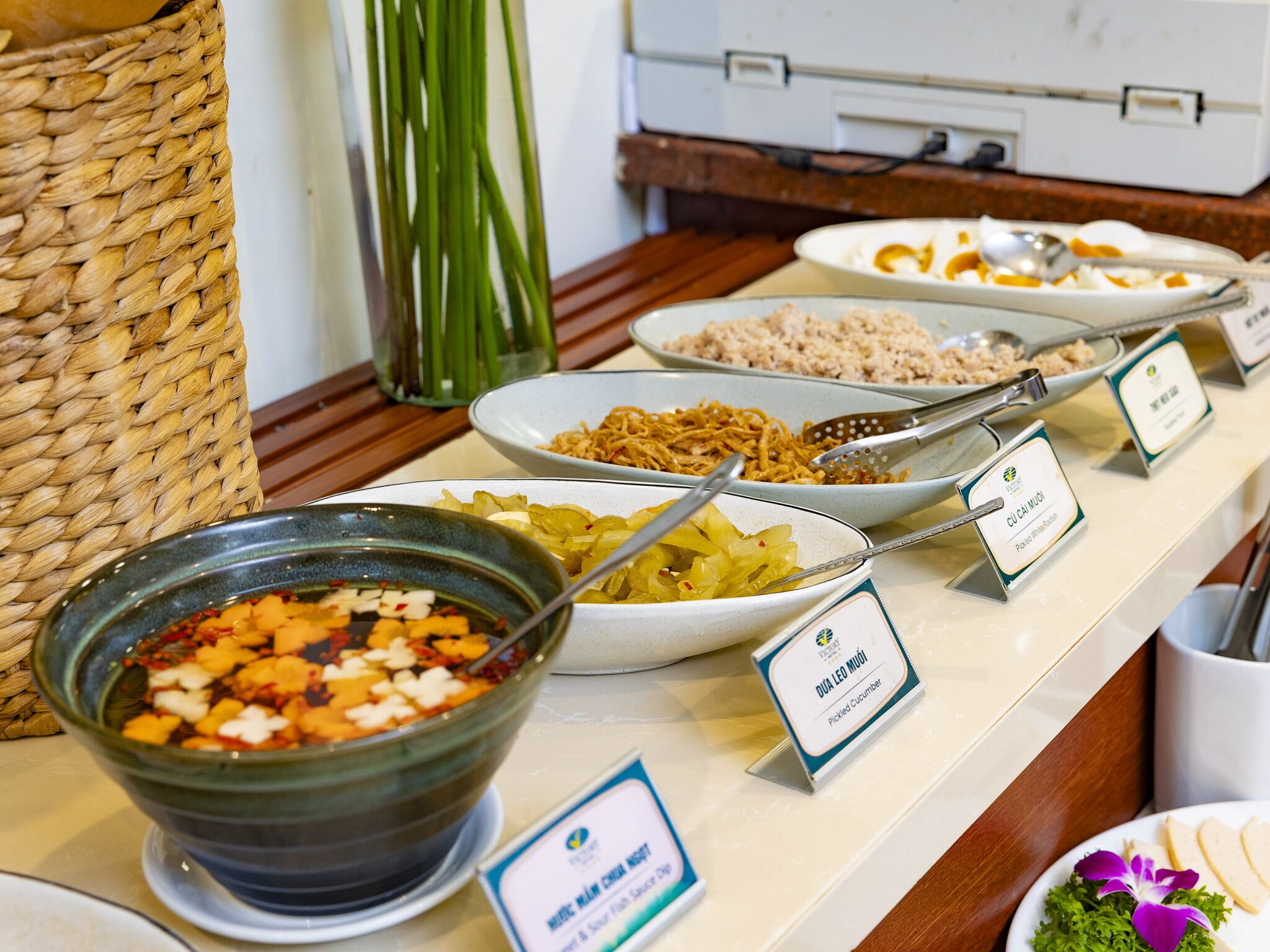 A buffet with various dishes including pickled cucumber, noodles, and a bowl of mixed vegetables.