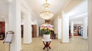 A lobby with a chandelier, a floral arrangement on a pedestal, and a signboard. - Victory Saigon Hotel (Ho Chi Minh City)
