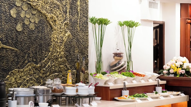 A buffet setup with various food items and condiments, a decorative wall, and a floral arrangement. - Victory Saigon Hotel (Ho Chi Minh City)