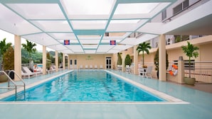 An indoor swimming pool with a clear ceiling, surrounded by lounge chairs and potted plants. - Victory Saigon Hotel (Ho Chi Minh City)