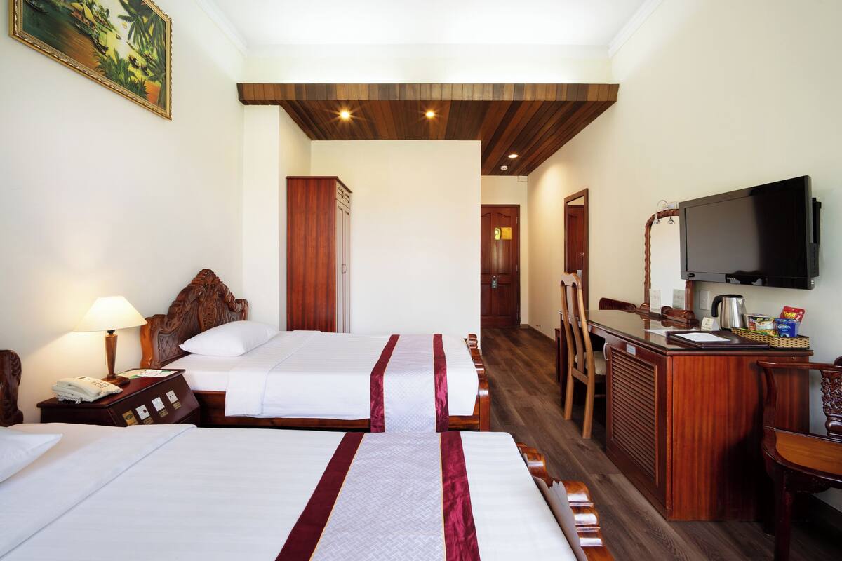 A hotel room with two beds, a desk with a television, and a wooden ceiling.