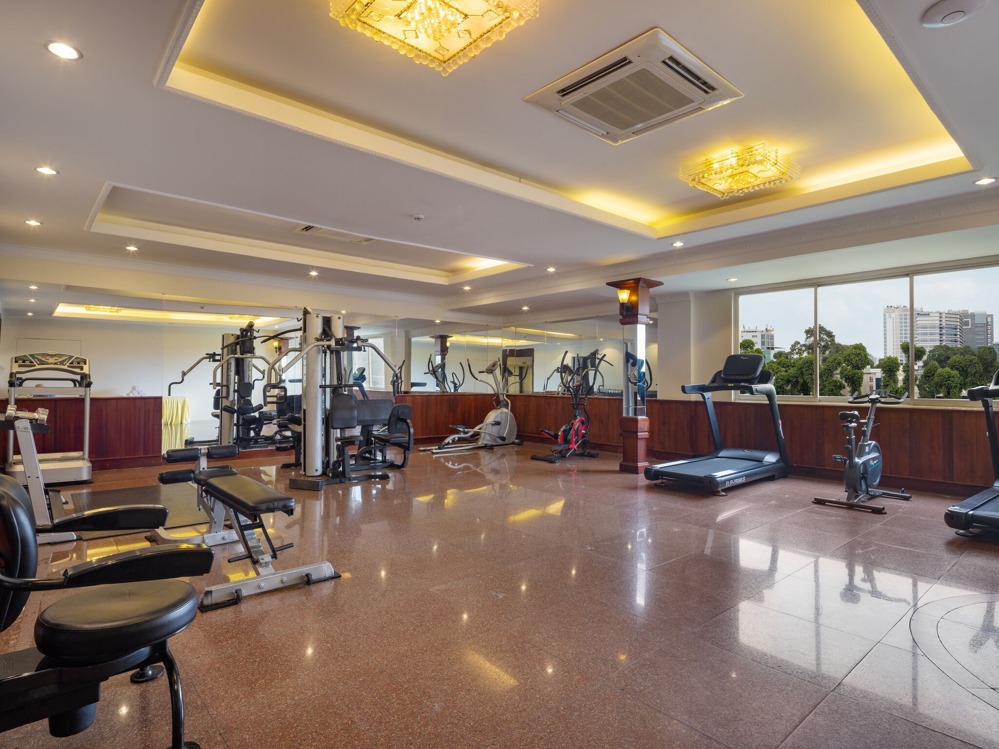 A well-lit gym with various exercise equipment, large windows, and a polished floor.