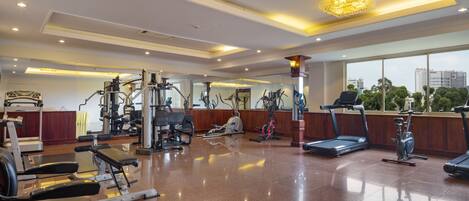 A well-lit gym with various exercise equipment, large windows, and a polished floor.