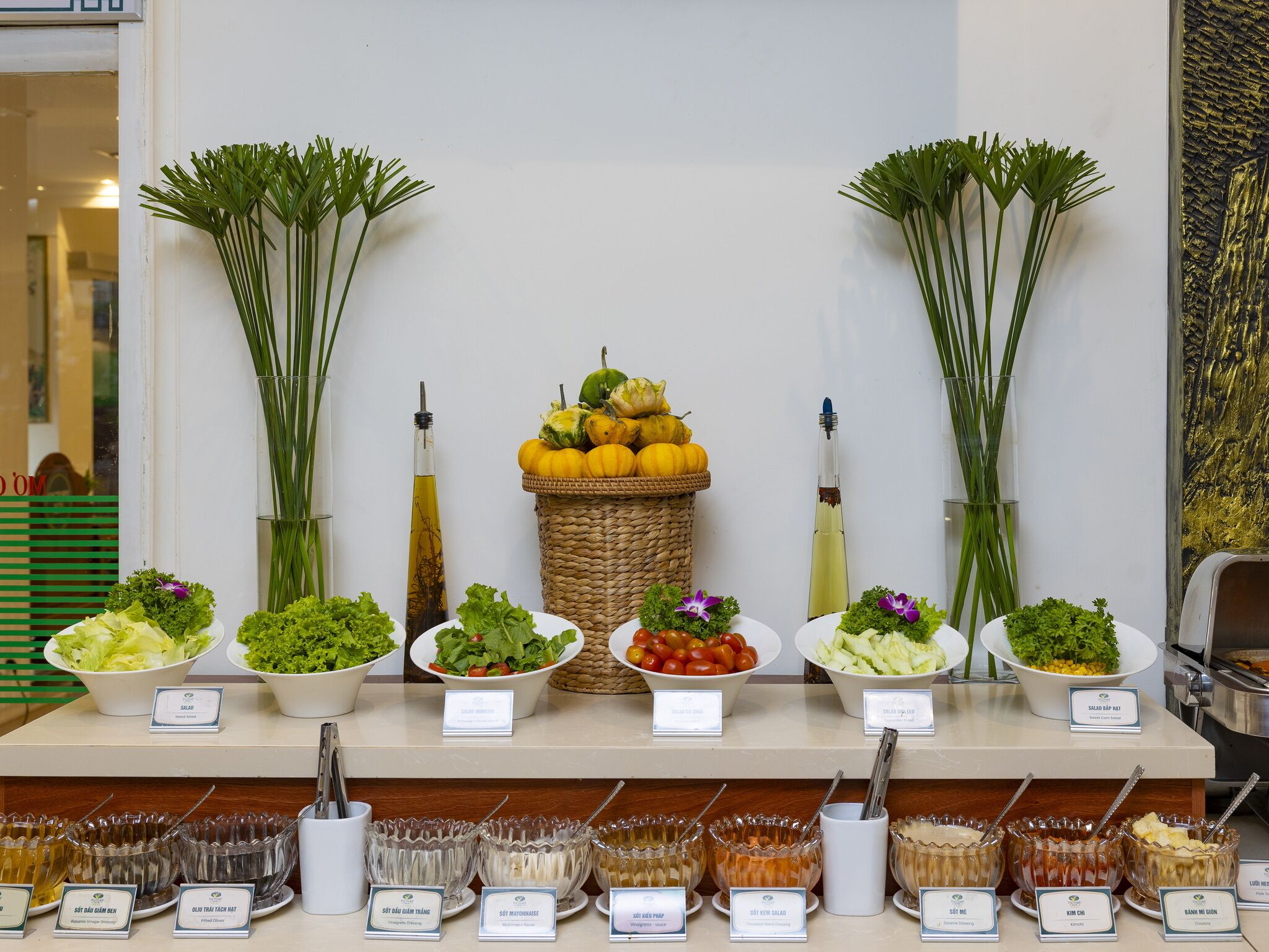 A buffet with various salads and condiments, including a bowl of mixed greens, a bowl of cherry tomatoes, and a bowl of corn salad.