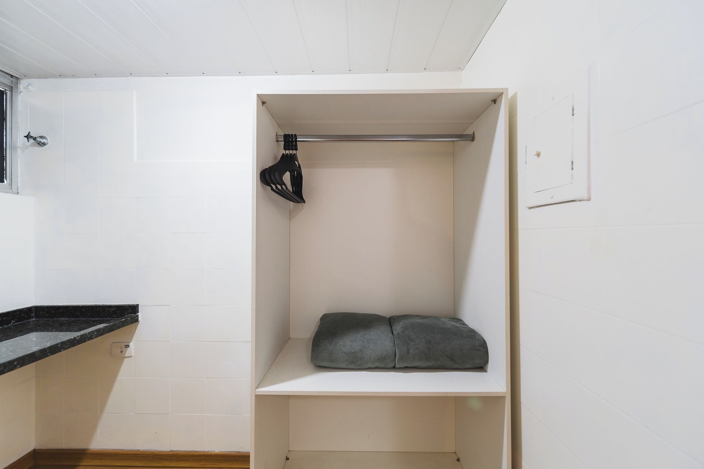 Un petit placard blanc, avec un porte-chaussures suspendu et une couverture grise pliée sur une étagère.