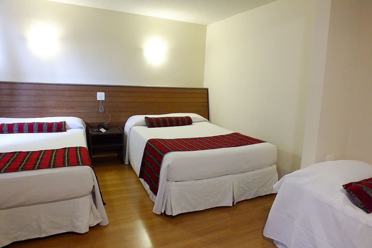 Habitación de hotel con dos camas individuales, cada una con una colcha a rayas rojas y negras, un cabecero de madera y una mesita de noche con un teléfono y una lámpara.