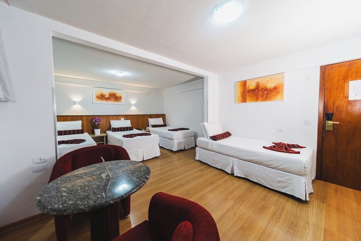 Una habitación de hotel con una cama, dos sofás blancos, una mesita y suelo de madera.