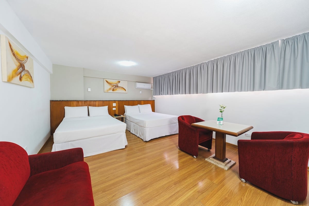 Una habitación de hotel con dos camas, una mesita pequeña y dos sillones rojos.