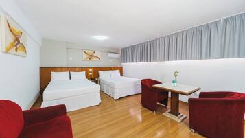 Quarto de hotel com duas camas, uma mesinha e duas poltronas vermelhas.
