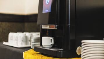 Una cafetera con pantalla digital, una taza y platos apilados sobre una mesa amarilla.