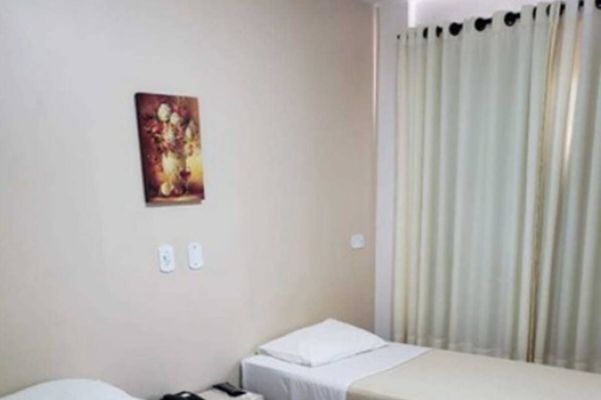 Une chambre d’hôtel avec deux lits simples, une table de chevet avec un téléphone, un interrupteur fixé au mur et un rideau.