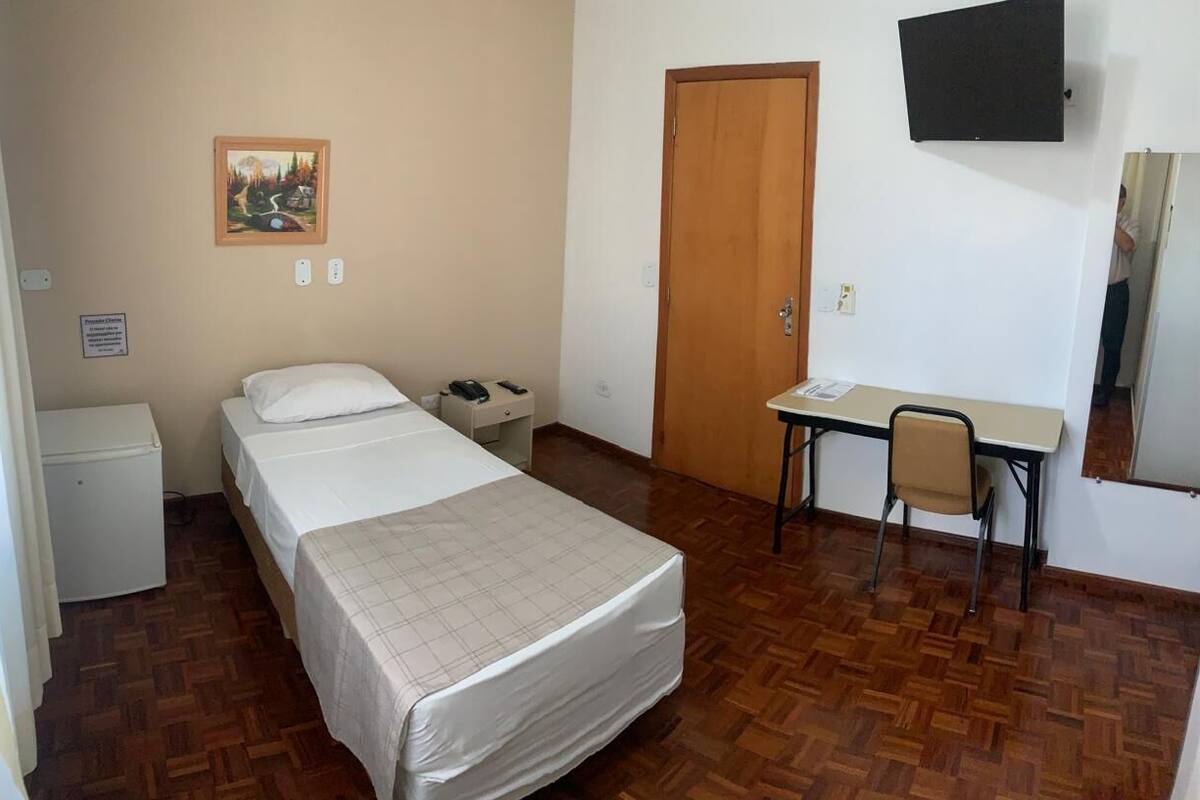 Une chambre à coucher avec un lit, un bureau, une chaise, une porte et un tableau accroché au mur.