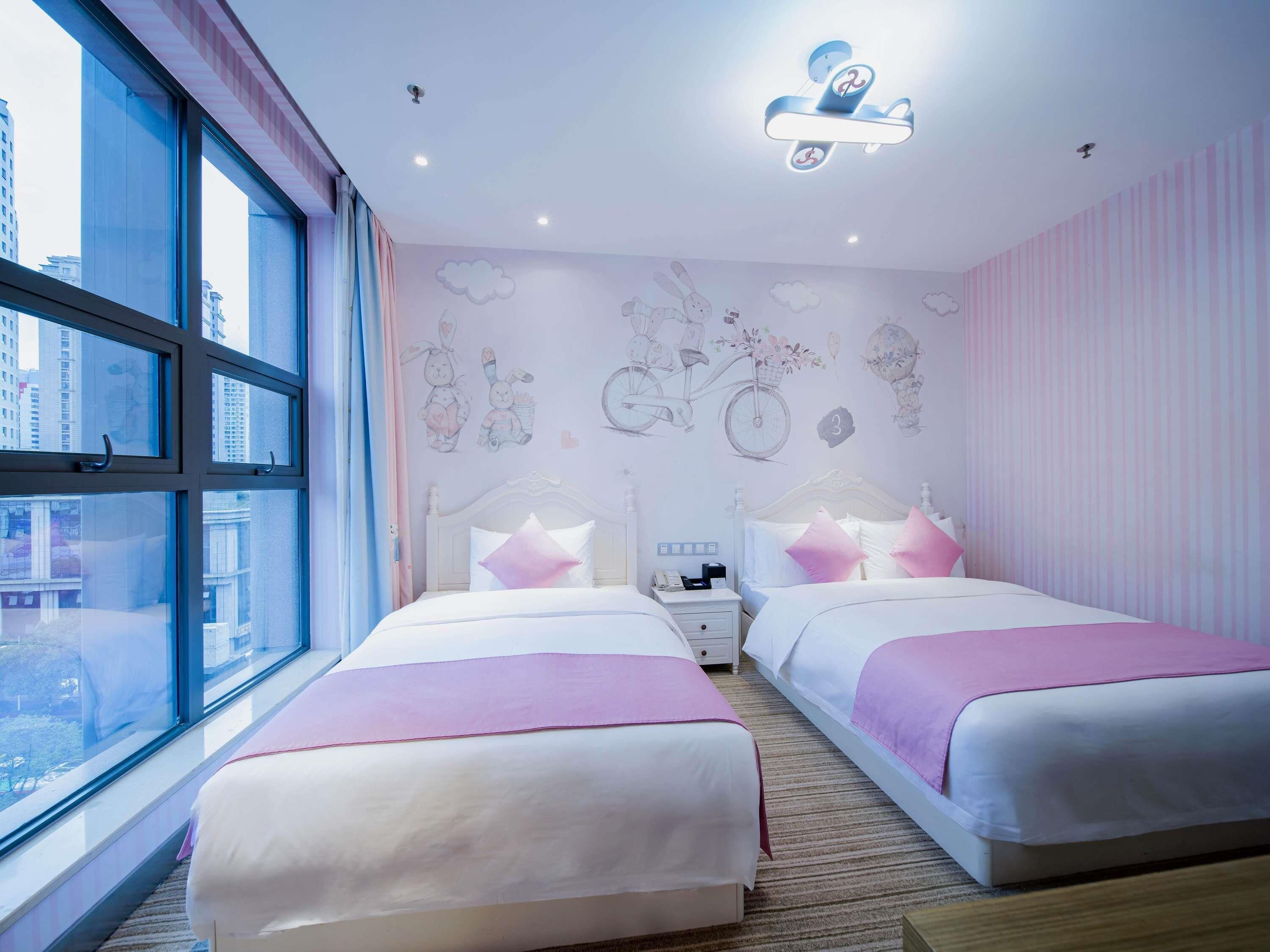 A hotel room with two beds, a large window, a wall mural, and a ceiling light fixture.