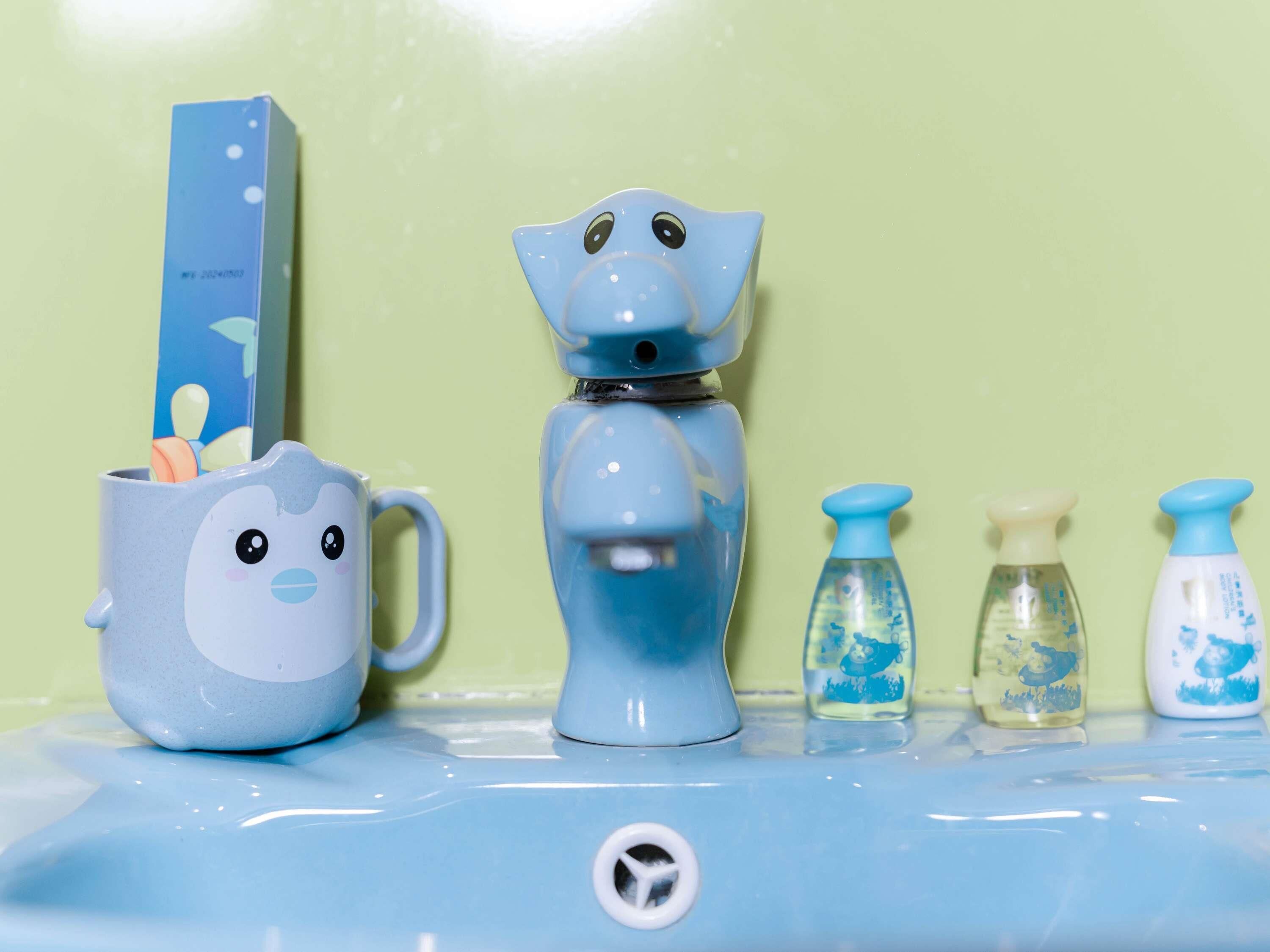 Un lavabo de salle de bain avec un robinet en céramique bleue, une tasse en céramique ornée d’un visage et deux distributeurs de savon.