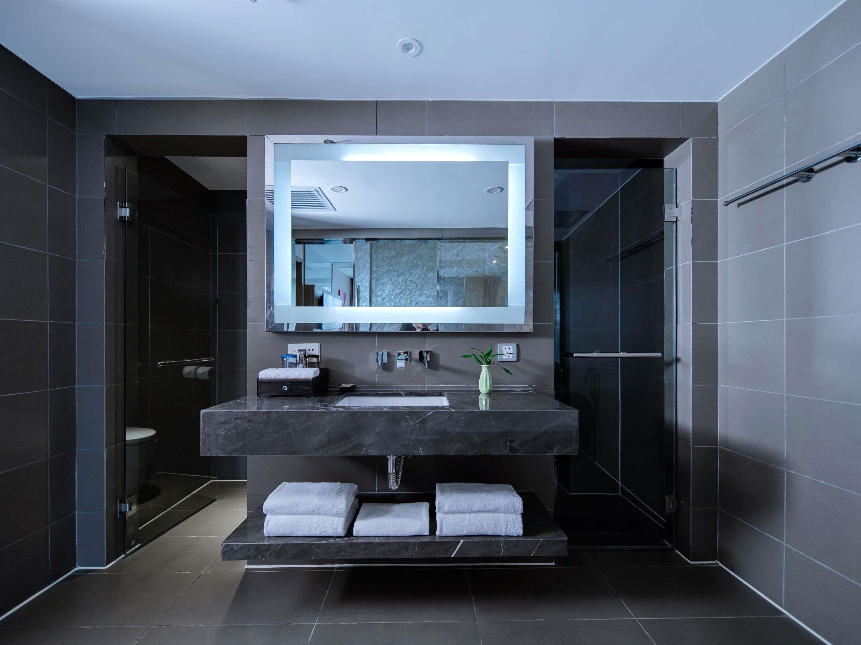A modern bathroom with a large mirror, dark tiles, a marble sink, and a towel rack.