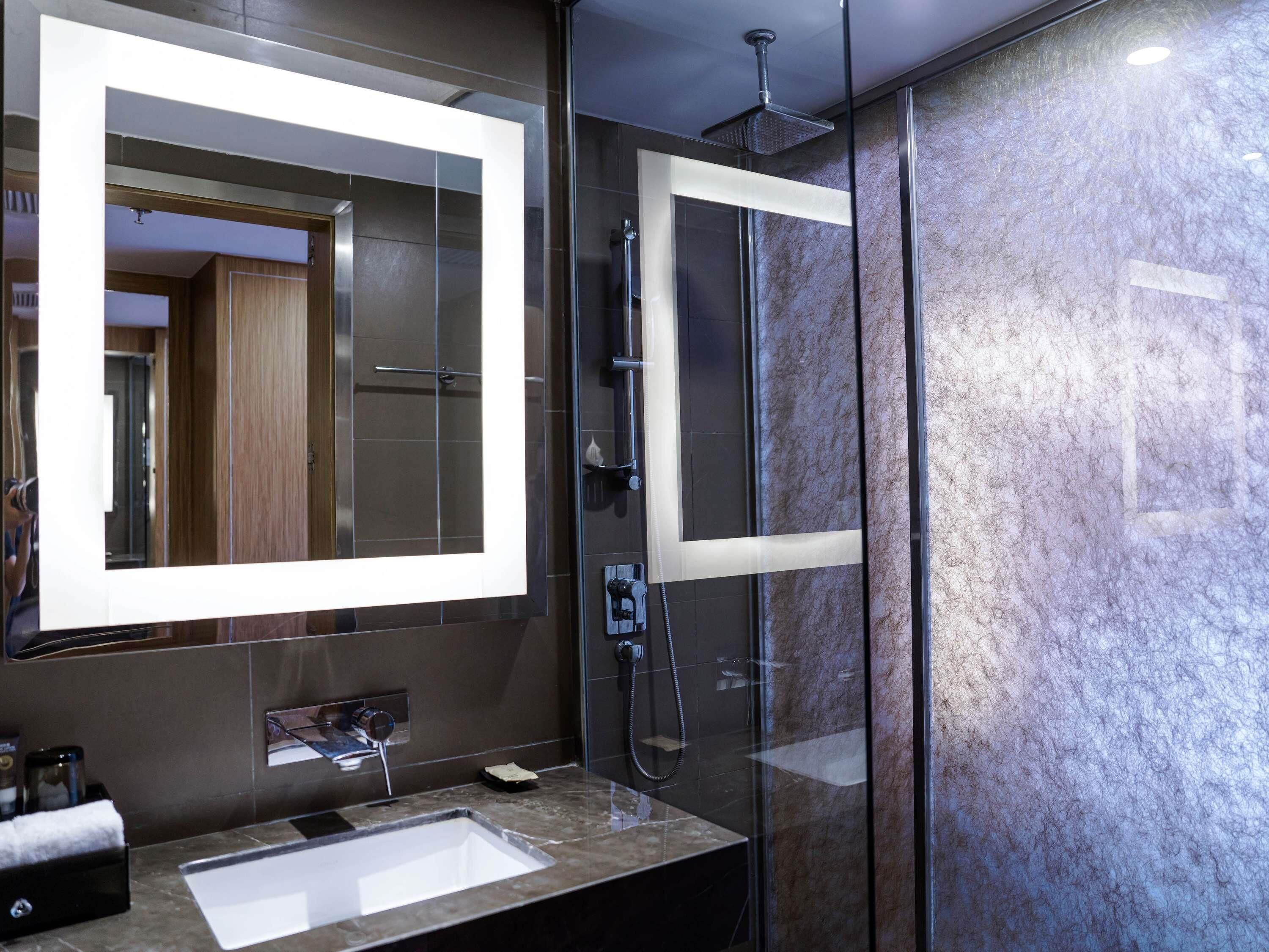 A modern bathroom with a large mirror, a glass shower enclosure, and a marble countertop.