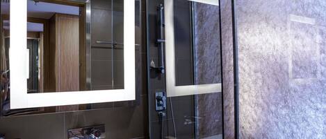 A modern bathroom with a large mirror, a glass shower enclosure, and a marble countertop.