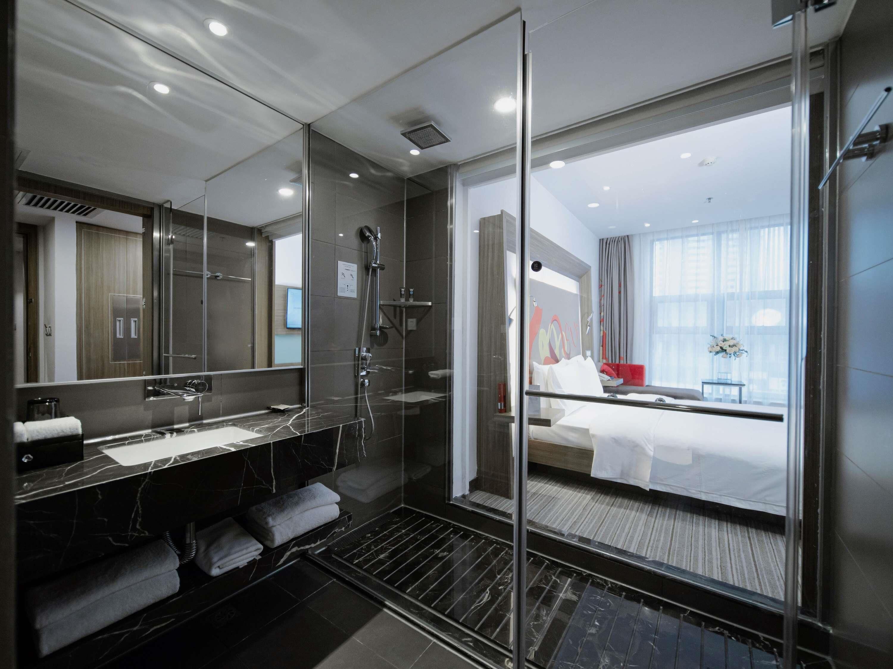 Ein modernes Hotelbad mit einer gläsernen Duschkabine, einem großen Spiegel und einem separaten Waschbereich.