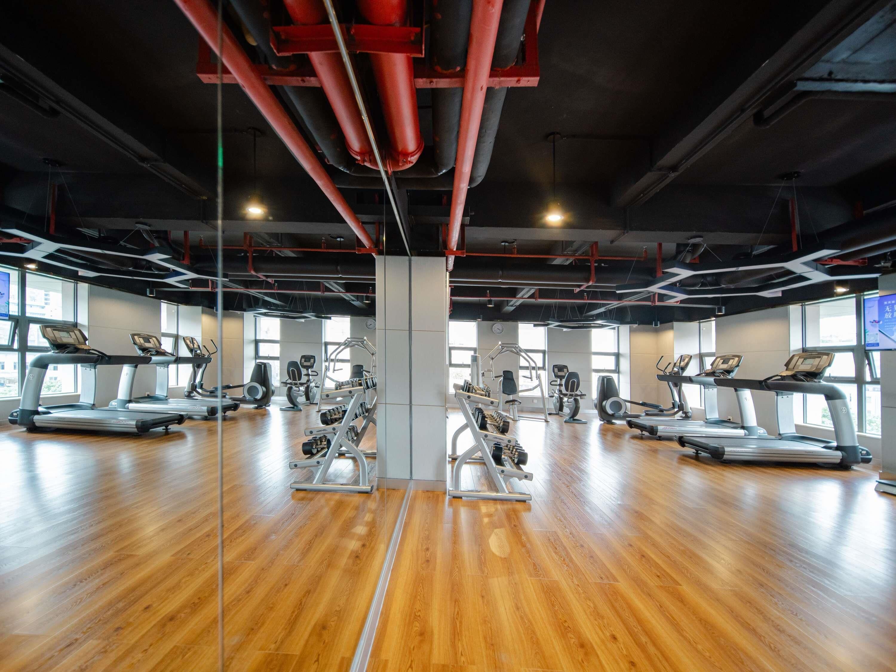 A gym with treadmills, weight machines, and a wooden floor.